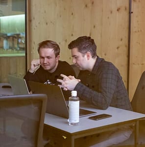 two men sitting at a table with a laptop